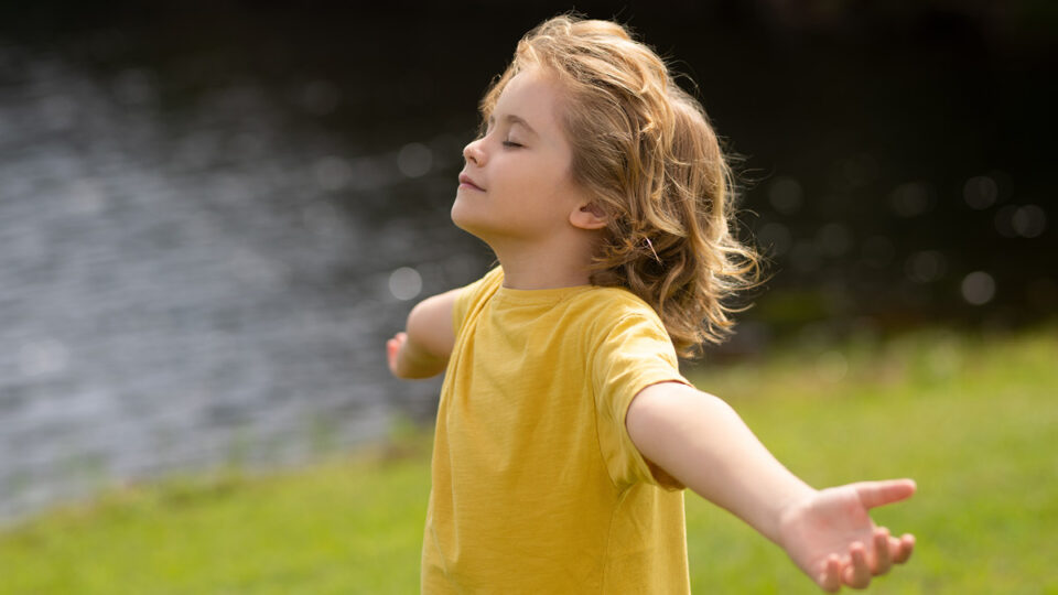 A girl standing up outside. her arms are outstreched and she has a peaceful expression