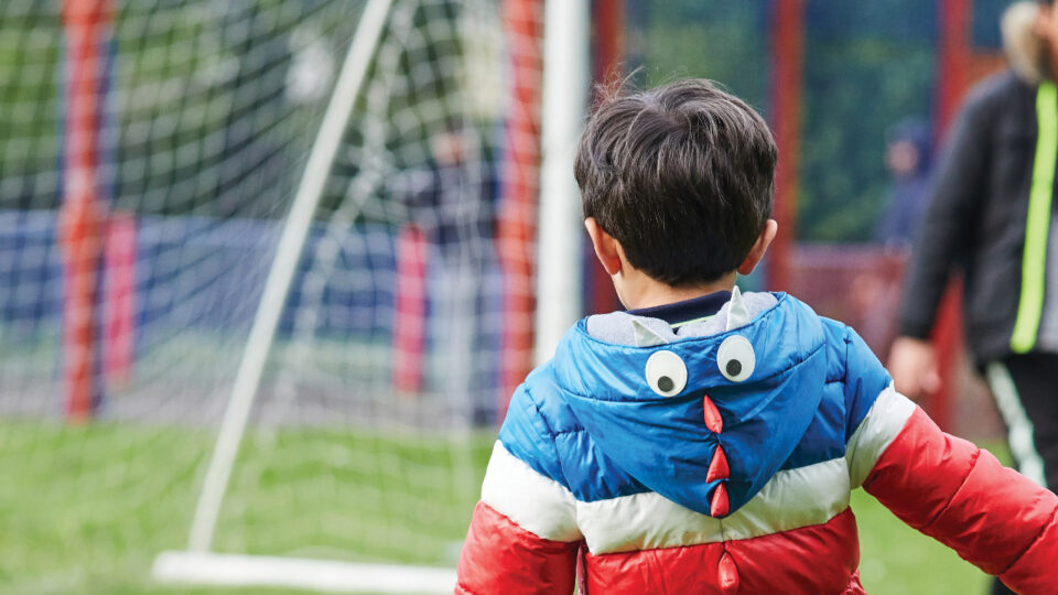 the back of a child wearing a coat. A football net is in the background