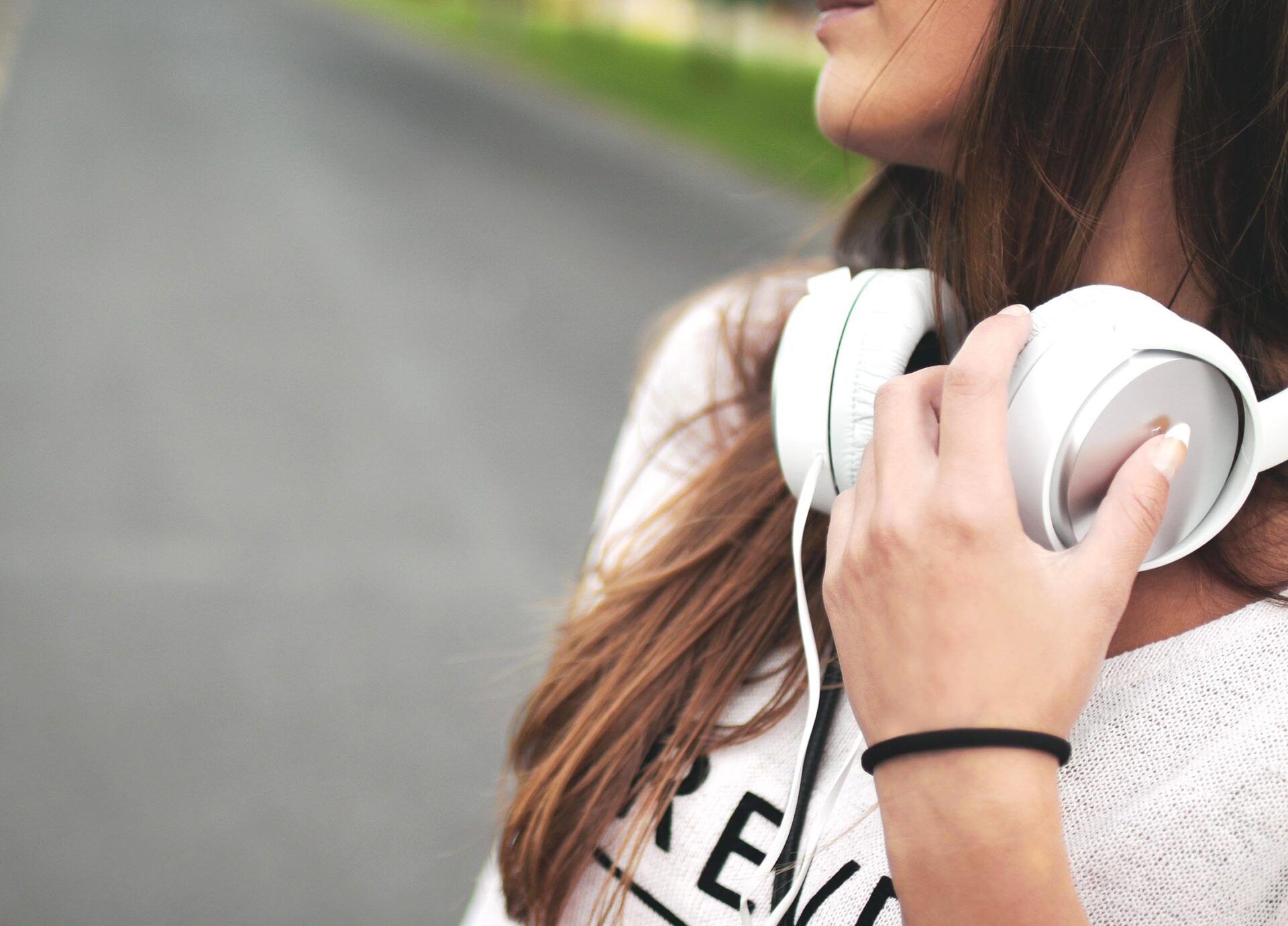 A girl holding a pair of white headphones around her neck