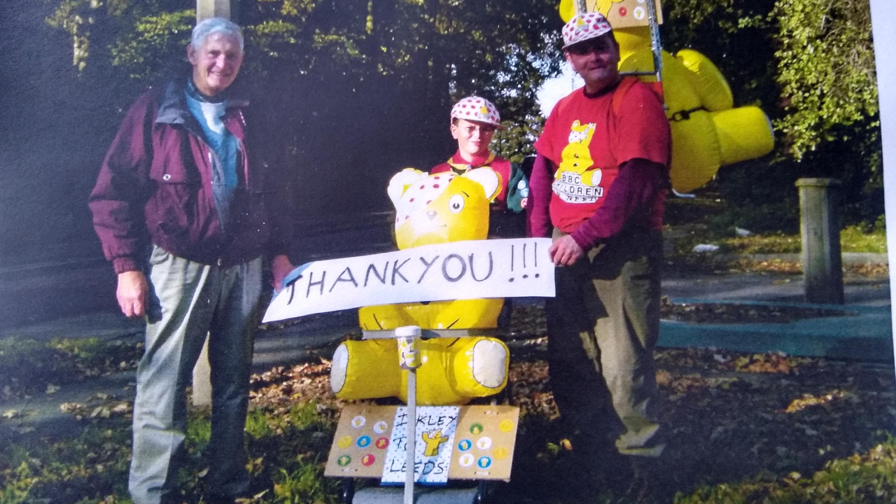 Stephen with his father and and Thank You paper banner in front of a large Pudsey Bear