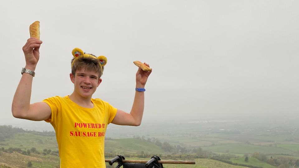 A boy on top of a hill holding pasties in his hand. His yellow t-shirt reads 'powered by pasties'