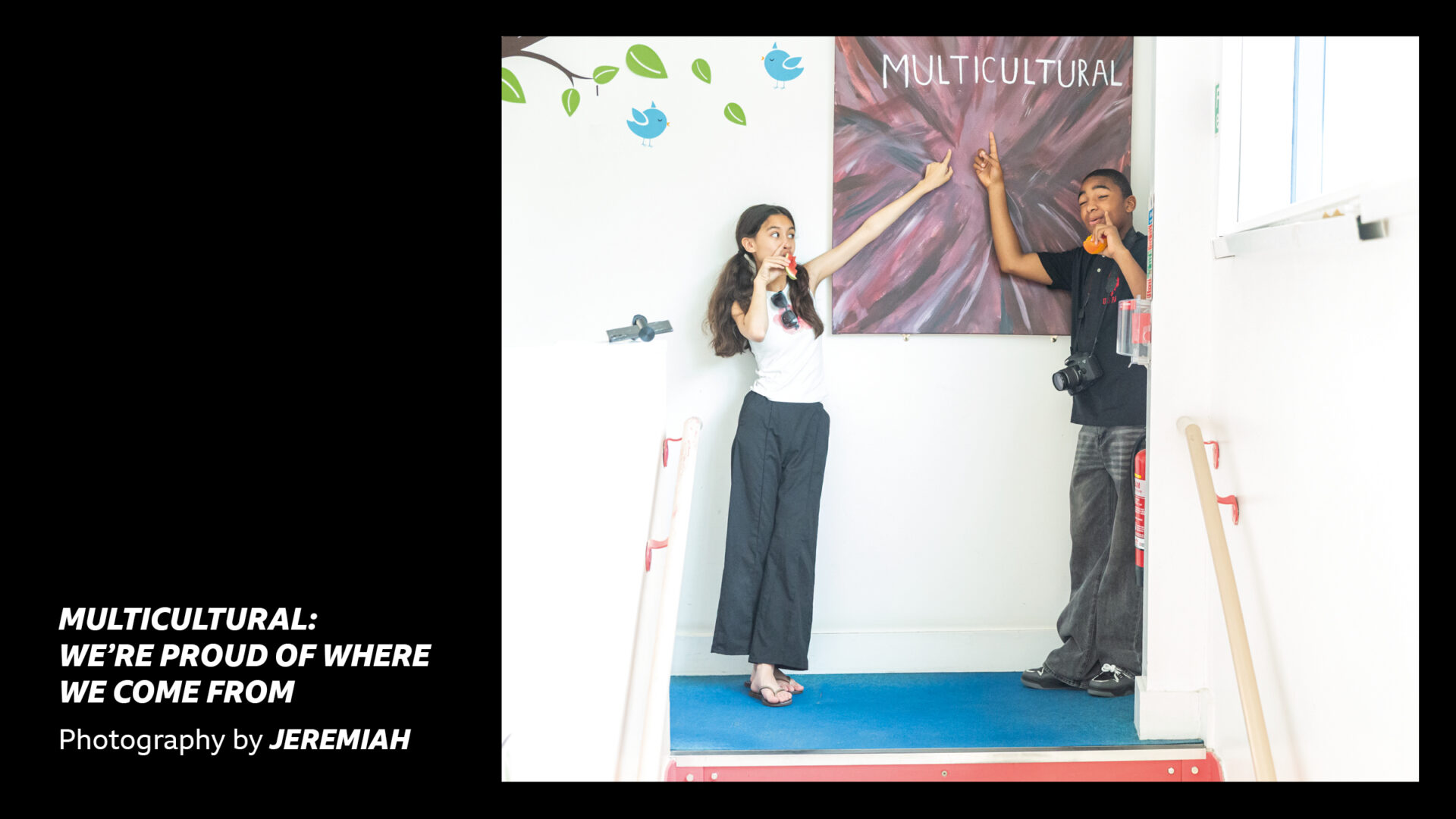 'Multicultural: We're proud of where we come from - Photography by Jeremiah' - Two young people pointing up at a sign which reads 'Multicultural'